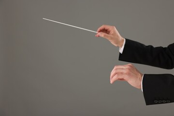 Professional conductor with baton on grey background, closeup. Space for text