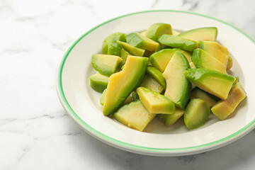 Cut ripe green avocado on white marble table, closeup