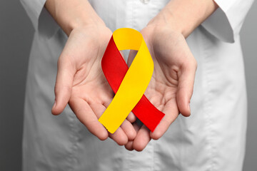 World Hepatitis Day. Doctor with yellow-red awareness ribbon on grey background, closeup