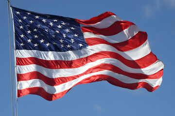 Fototapeta premium The American flag waves crisply in the wind, with sharp fabric movement set against a vast clear blue sky on Flag Day