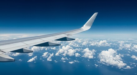 Fototapeta premium Photo of Airplane Wing with Blue Sky and Fluffy White Clouds