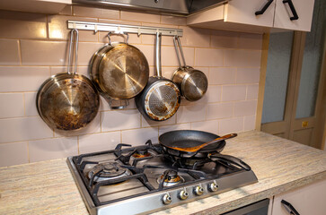 Domestic kitchen with greasy stainless steel pots and pans hanging on a tiled wall, above a dirty...
