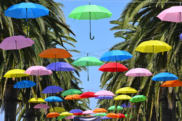 Colorful umbrellas suspended by wire between rows of palm trees.