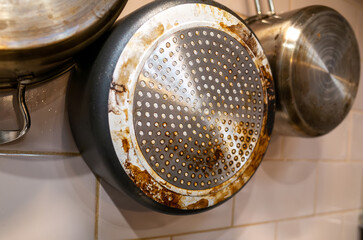 Close-up of a dirty frying pan with heavy grease buildup and burnt stains on the metal bottom,...