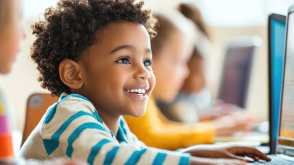 A young child wearing a striped shirt, sitting at a desk with a laptop, smiling and looking at the screen.