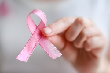 Hand delicately holding a pink ribbon symbolizing international breast cancer awareness and support