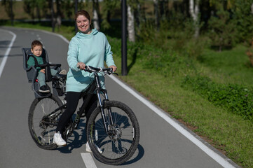 Caucasian woman riding a bicycle with her toddler son sitting behind her in a child seat. 