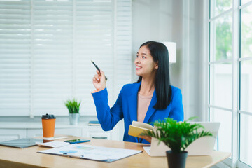 An Asian businesswoman in a blue blazer celebrates with joy while looking at her smartphone. She...