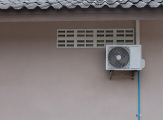 The air conditioner is installed outside the house on the eaves of the gray wall.