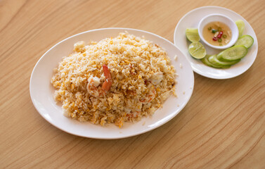 Shrimp fried rice in white plate with condiments placed on wooden table