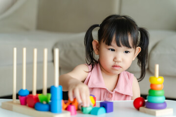 3 year old girl having fun playing with colorful geometric shape wooden blocks educational toys at...