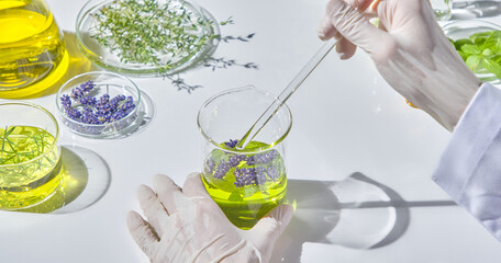 A researcher's hand is stirring a bright green natural oil mixture in a glass beaker with a glass...