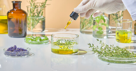 Hand of a lab technician gently mixing essential oils and herbal solutions with natural ingredients like lavender and leaves. Front view