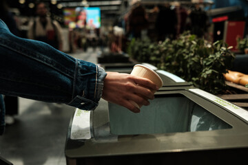 Person throwing paper cup in recycling bin at public place