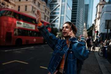Young woman hailing taxi while talking on phone in london