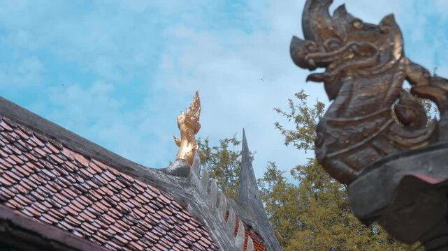 Beautiful wooden carved and gilded chofahs - traditional Thai serpent-shape decorative elements are guarding red tile roofs of Wat Na Phra Meru Buddhist temple in Ayutthaya, Thailand. Shot in motion