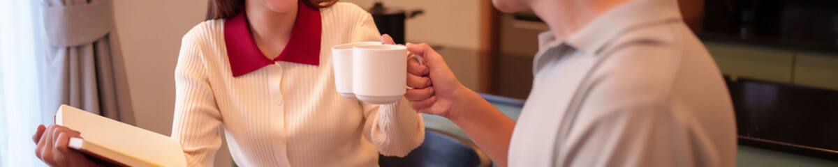 Asian Woman and Man Toasting Coffee Mugs in Kitchen Setting Enjoying Morning Routine Together Celebrating Cheerful Moment with Warm Beverages