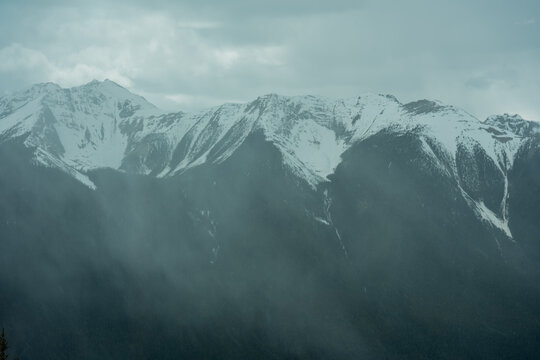 Snowy peaks are wrapped in mist under a gray sky.