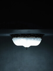 Vertical photo of vintage ceiling lamp with frosted glass glowing in a dark interior room. Ornate metal details create a nostalgic and moody ambiance.
