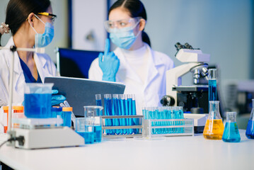 Two Asian female biotechnologists in lab coats conduct research, handle glassware, and test...