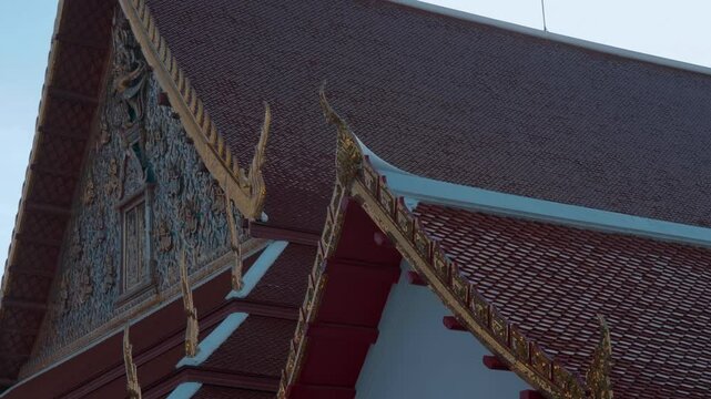 Traditional Thai Buddhist temple with beautiful red tiled roof with magnificent chofas in Thai architectural style. Shot in motion