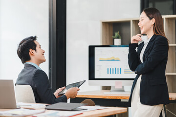 Business professionals discussing dashboard data in modern office, smiling and engaging in teamwork with digital tablet and computer screen displaying analytics in background