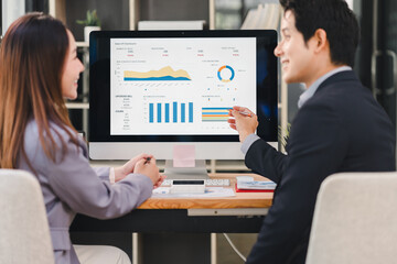 Business professionals discussing data analysis at modern office desk with dashboard charts and graphs displayed on computer screen, showing teamwork and positive collaboration