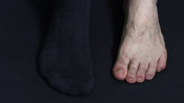 A man takes off his dark socks against a dark background, top view, close-up.