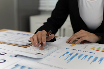 A confident young businesswoman sits at her laptop in a modern office, focused on planning strategies. Surrounded by documents, technology, and ideas, she collaborates with colleagues, embodying creat