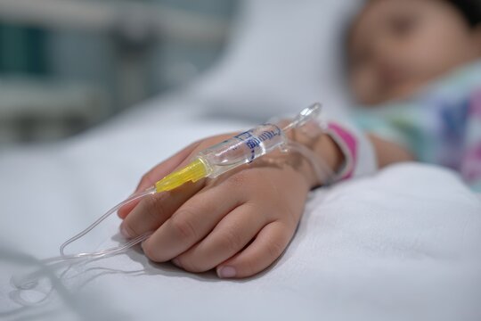 Child's hand with IV in hospital bed.