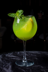 A vibrant green cocktail with mint and citrus awaits on a dark table, inviting sips