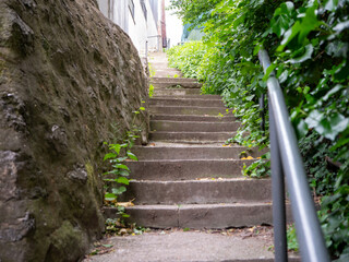 Concrete outdoor stairs surrounded by green foliage and a stone wall, leading uphill in an urban...