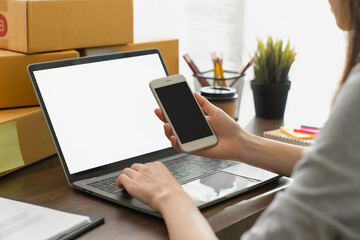 Hand holding a blank white screen smartphone and laptop on table, for putting advertising to promote.
