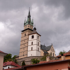Fototapeta premium View of the Church of St. Catherine and clock tower within Kremnica Castle, rising above town roofs and medieval fortifications, with a dramatic sky in the background.