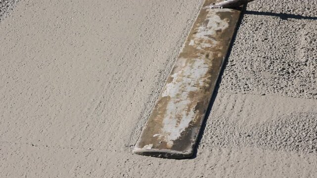 Worker smoothing fresh concrete with trowel close-up footage of a construction worker using a long-handled trowel to level and smooth a freshly.