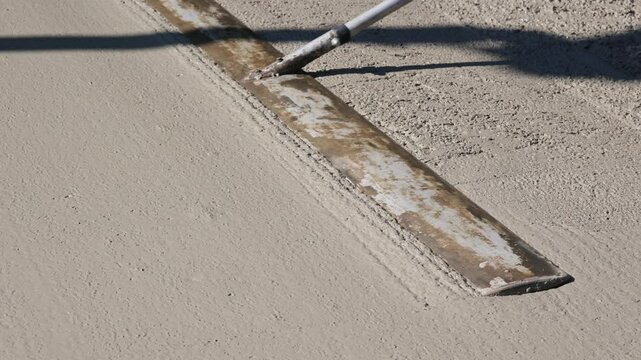 Worker smoothing fresh concrete with trowel close-up footage of a construction worker using a long-handled trowel to level and smooth a freshly.
