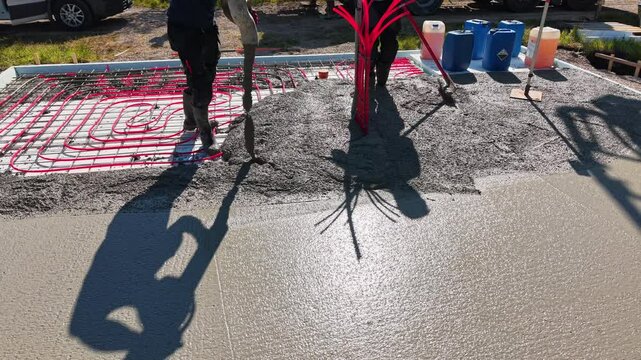Pouring concrete over underfloor heating system &ndash; construction process Video of a construction worker in rubber boots pouring concrete over red underfloor.