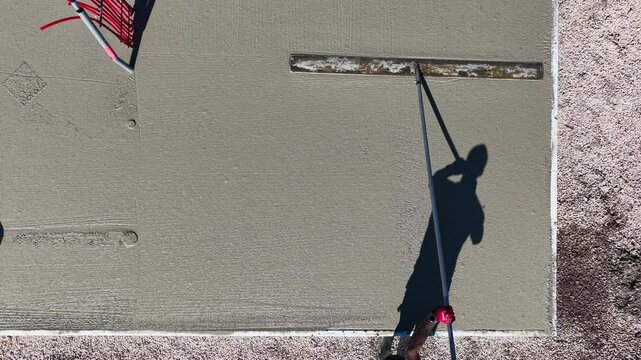 Drone video of worker leveling concrete slab with long trowel Aerial video showing the shadow of a construction worker using a long-handled trowel to smooth freshly.