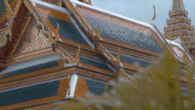 Roof of traditional Thai style paved with blue and orange tiles and chofas of the Reclining Buddha (Sleeping Buddha) Buddhist Temple in Bangkok. Shot in motion