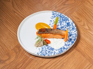 Grilled salmon fillet with creamy sauce and vegetables served on a blue patterned ceramic plate