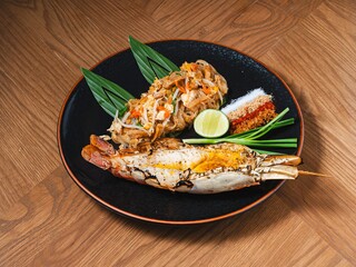 Pad Thai with grilled river prawn served on black plate with traditional Thai condiments