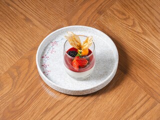 Panna cotta in glass topped with berry sauce and fresh fruits on ceramic plate
