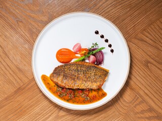 Seared fish fillet with tomato herb sauce and gourmet vegetable garnish on white plate