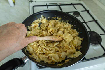 hand stirring cabbage noodles in a wok with a wooden spoon