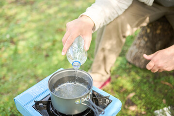 Unknown person pouring drinking water into a pot as part of the process of cooking outdoors, in a portable gas stove, while camping. Selective focus on water.