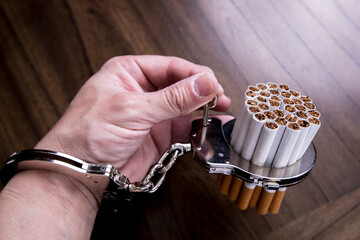 Cigarettes attached to a handcuff and hand, as in attached to your self and cant quit