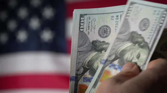 Stack of american hundred dollar bills in a hand against the background of the american flag, close up. Concept of finance, business, economics and reliability of money