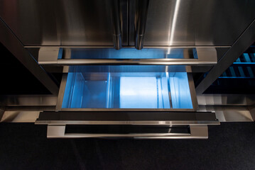 Open stainless steel freezer drawer with internal LED lighting