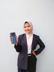 Young Hijabi Entrepreneur Wearing Formal Suit Presenting Mobile Phone Display, Standing Against...