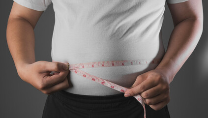 Overweight or obese man with abdominal fat using a tape measure to check his waist size, Health and medicine concept He is on a diet and losing weight